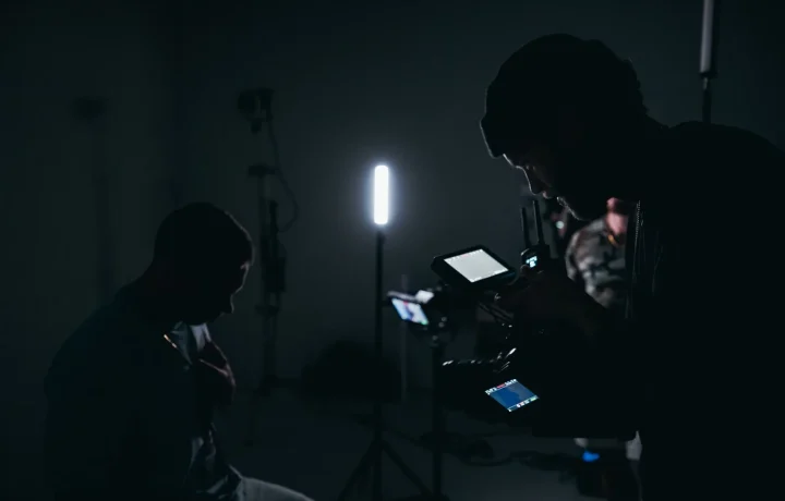 A cinematographer using a camera in a low-light studio, showcasing the importance of teleprompters for video formats