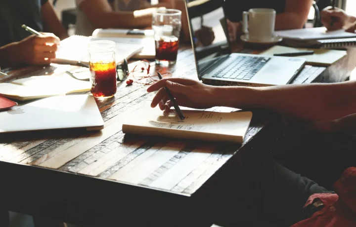 A group of adults collaborating in an office meeting, sharing essential tips with notes and laptops
