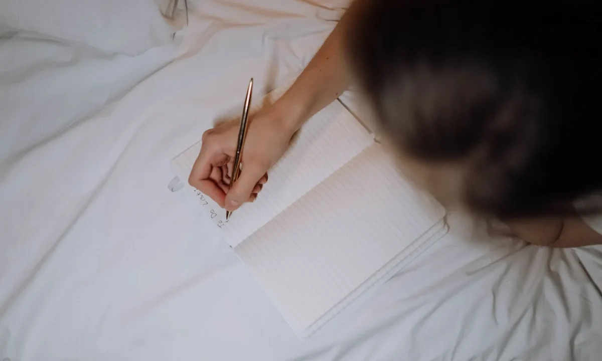 A person writing down essential tips for step-by-step planning in a notebook on a bed