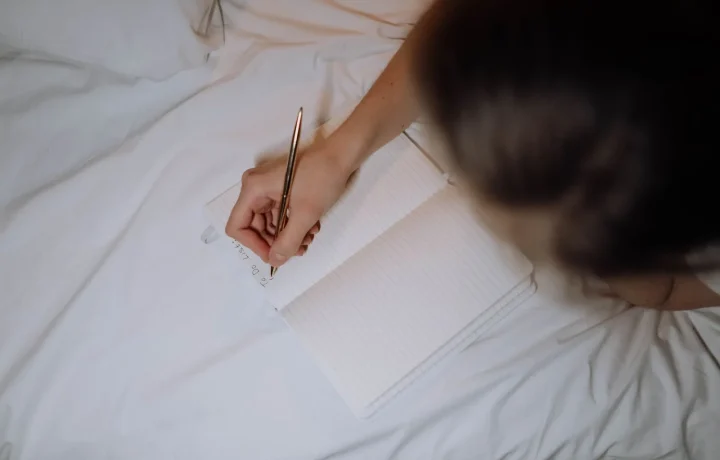A person writing down essential tips for step-by-step planning in a notebook on a bed