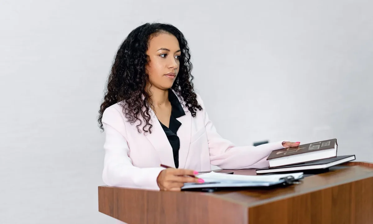A professional black woman lawyer confidently presenting at a podium surrounded by legal books to illustrate on-camera
