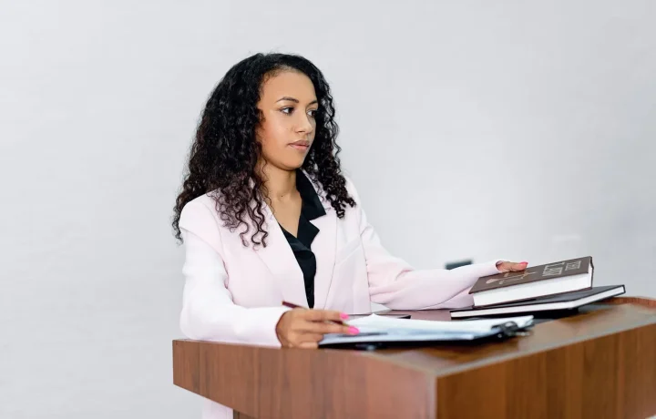 A professional black woman lawyer confidently presenting at a podium surrounded by legal books to illustrate on-camera