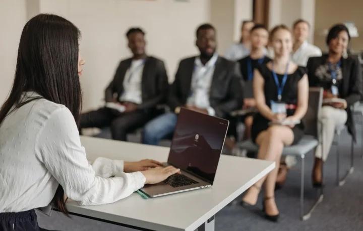 A professional woman confidently presenting to a diverse group of colleagues in a modern office setting