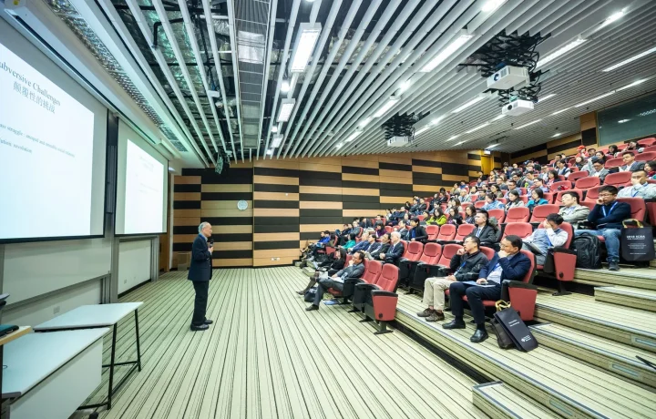 A speaker presents confidently to an engaged audience in a sleek auditorium, highlighting teleprompters in corporate training