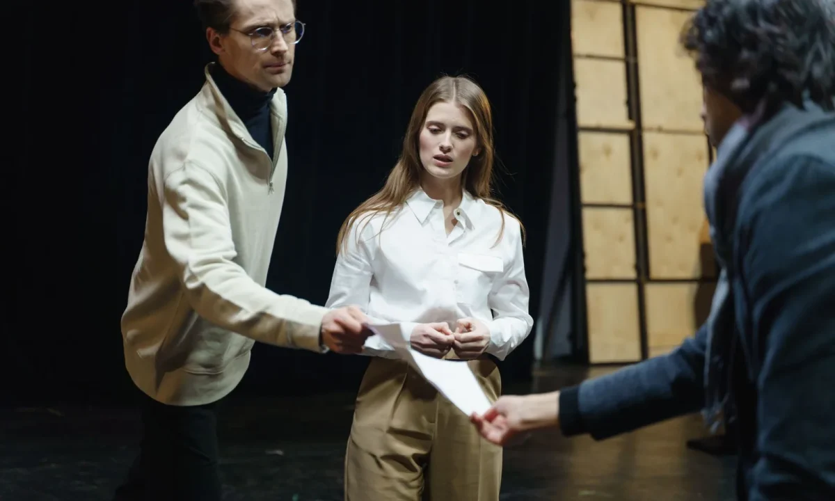 Actors rehearse on stage, exchanging scripts, showcasing the art of script writing for teleprompters in action