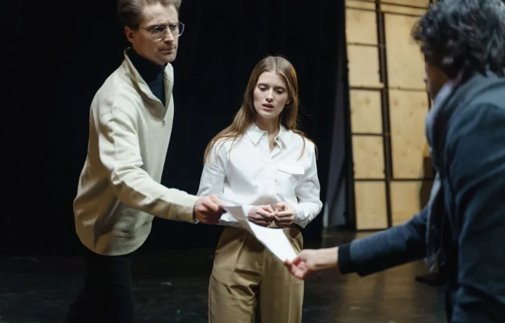 Actors rehearse on stage, exchanging scripts, showcasing the art of script writing for teleprompters in action