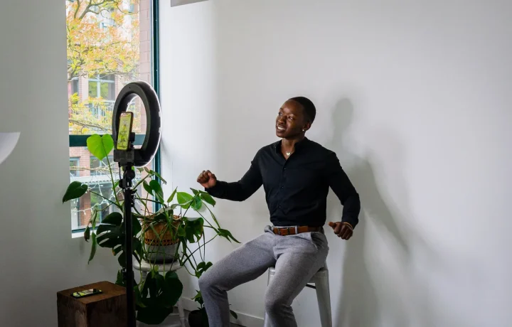African American man using a smartphone and ring light to create content in a stylish modern room for live streaming