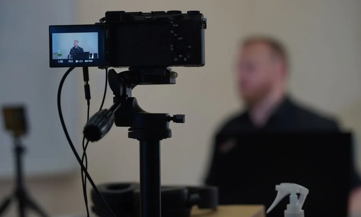 Close-up of a camera setup with a blurred speaker, illustrating the use of a teleprompter for video formats