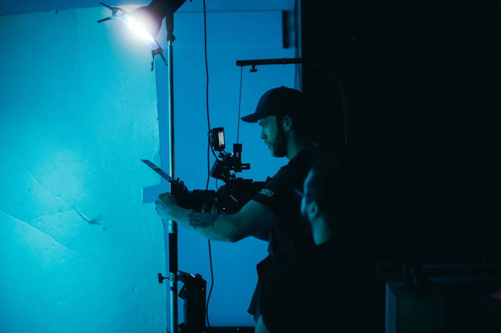 Man adjusting a camera on a film set under moody studio lighting before writing his teleprompter script