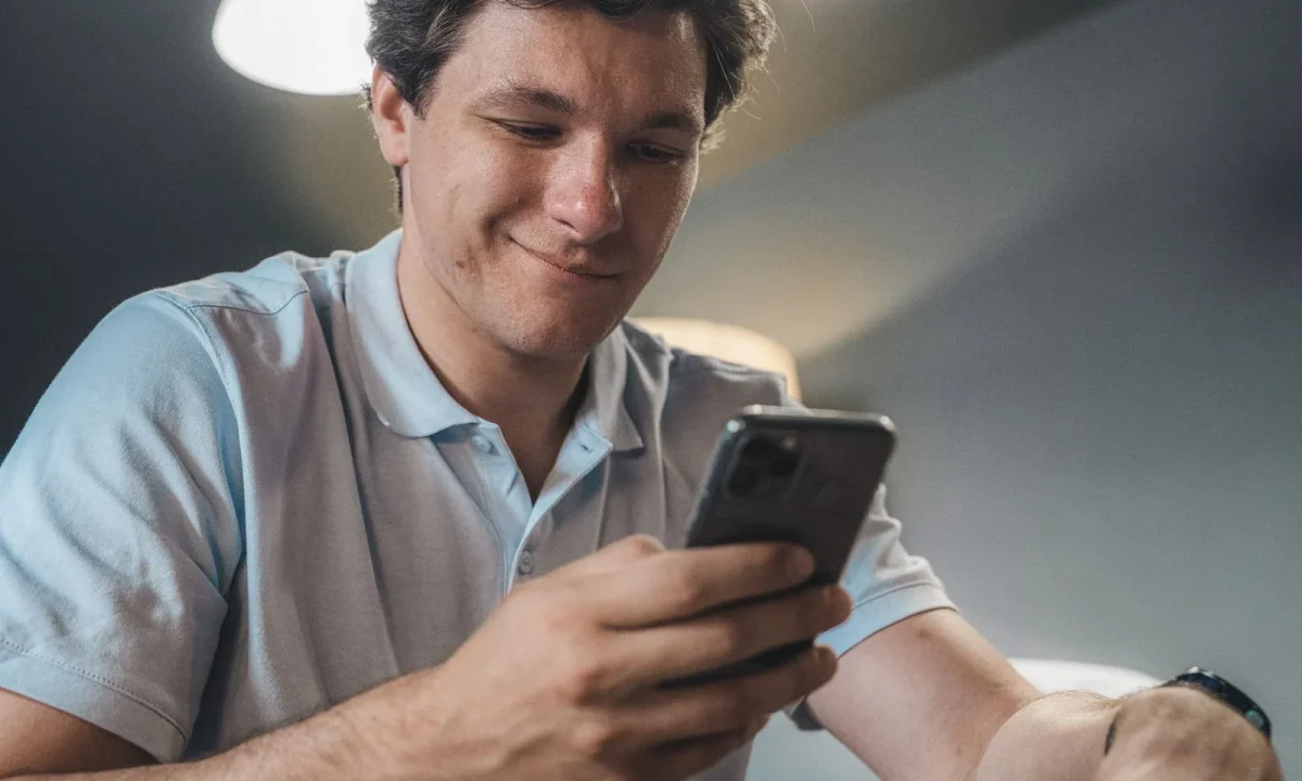 Man in a blue polo shirt smiling as he reads a script on his phone, a teleprompter app comparison starting point