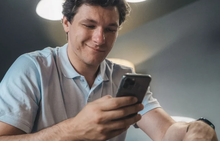 Man in a blue polo shirt smiling as he reads a script on his phone, a teleprompter app comparison starting point