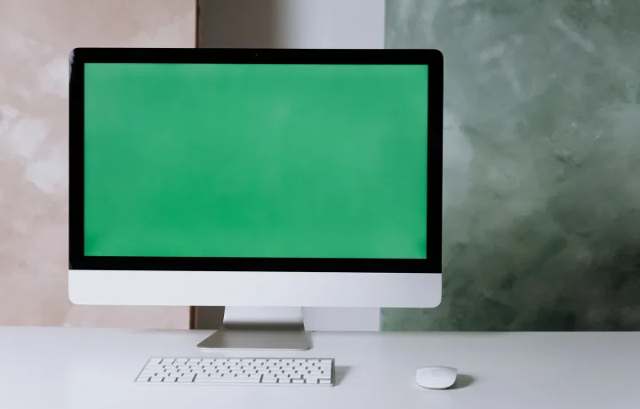 Minimalist workspace with a computer and green screen, illustrating the future of teleprompters technology