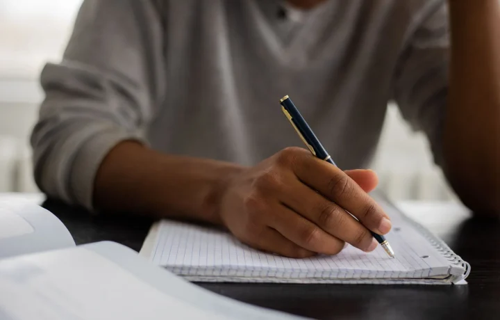 Unrecognizable African American male taking notes in workbook, emphasizing essential tips for effective studying