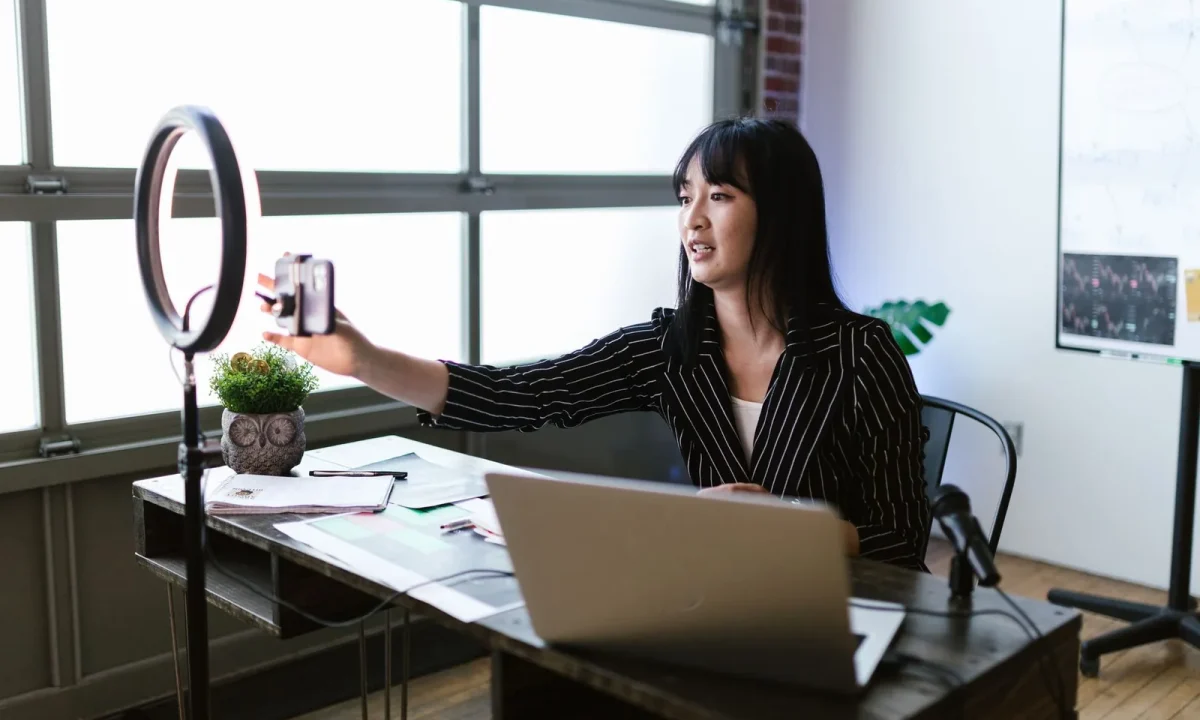 Woman in an office using a smartphone and ring light to demonstrate live streaming teleprompter techniques