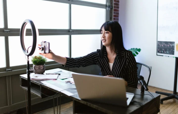 Woman in an office using a smartphone and ring light to demonstrate live streaming teleprompter techniques