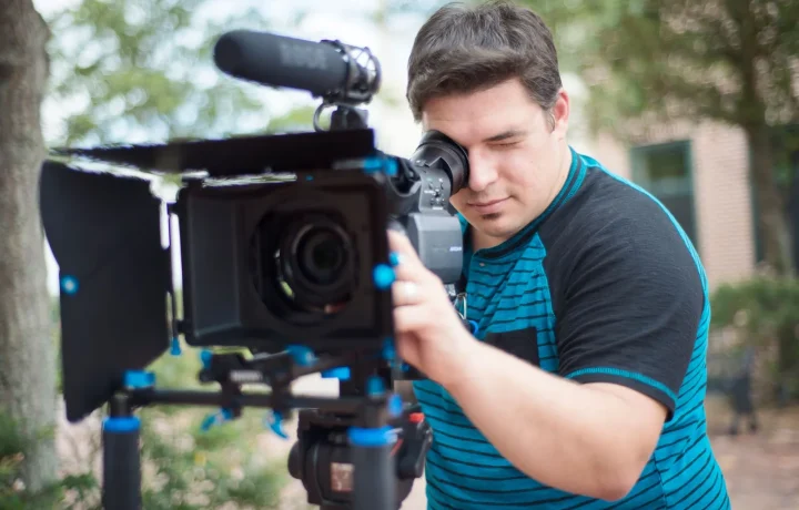 Young male videographer operating a professional camera outdoors, demonstrating the use of teleprompter apps in action