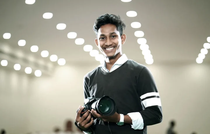 Young man exuding on-camera confidence while holding a camera with modern lights in the background